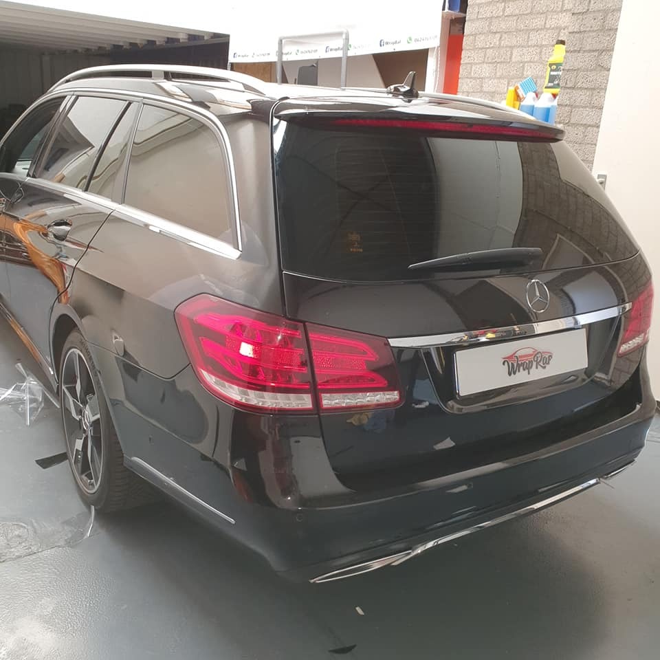 Ciemne szyby w tylnej części czarnego kombi marki Mercedes, widoczny logotyp firmy na klapie bagażnika.