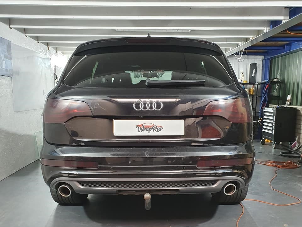 Ciemnoszary SUV marki Audi z przyciemnionymi tylnymi szybami i lampami, widok z tyłu, w tle warsztat z narzędziami i sprzętem.