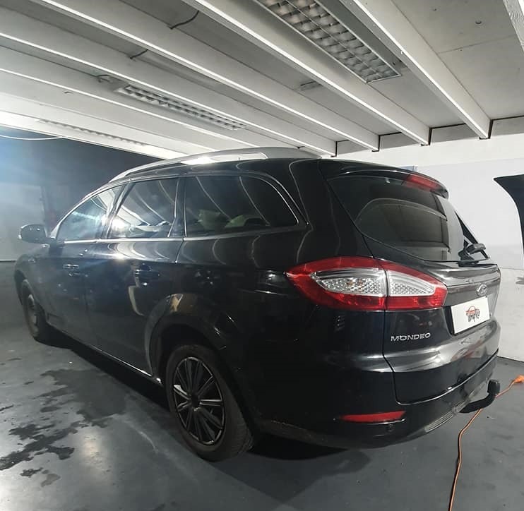 Czarne kombi Ford Mondeo, widok z tyłu pod kątem, w jasnym garażu z widocznymi lampami sufitowymi. Szyby wydają się być ciemniejsze niż standardowe.