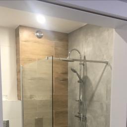 Mc Rem-House Remonty-Wykończenie Wnętrz - Nowoczesna kabina prysznicowa walk-in z deszczownicą i baterią termostatyczną, wykończona płytkami w odcieniach beżu i szarości, widoczna przez framugę drzwi.