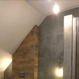 Mc Rem-House Remonty-Wykończenie Wnętrz - Ukośna łazienka z szarymi i drewnopodobnymi płytkami, widoczne niedokończone podłączenie oświetlenia.