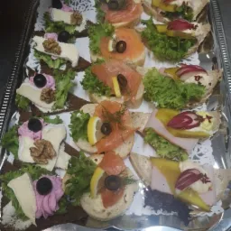 Srebrna taca z różnorodnymi kanapkami: z łososiem, serem camembert, szynką, dekorowane sałatą, cytryną, oliwkami i orzechami włoskimi.