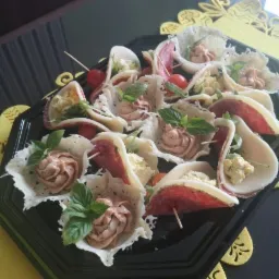 Elegancka taca z przekąskami: kruche koszyczki z różnymi farszami, salami i pomidorkami cherry, udekorowane świeżą bazylią.