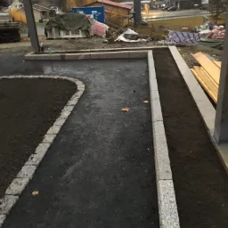 Przygotowany teren pod trawnik i ścieżkę z obrzeżami granitowymi, widoczne materiały budowlane w tle, jesienna sceneria.