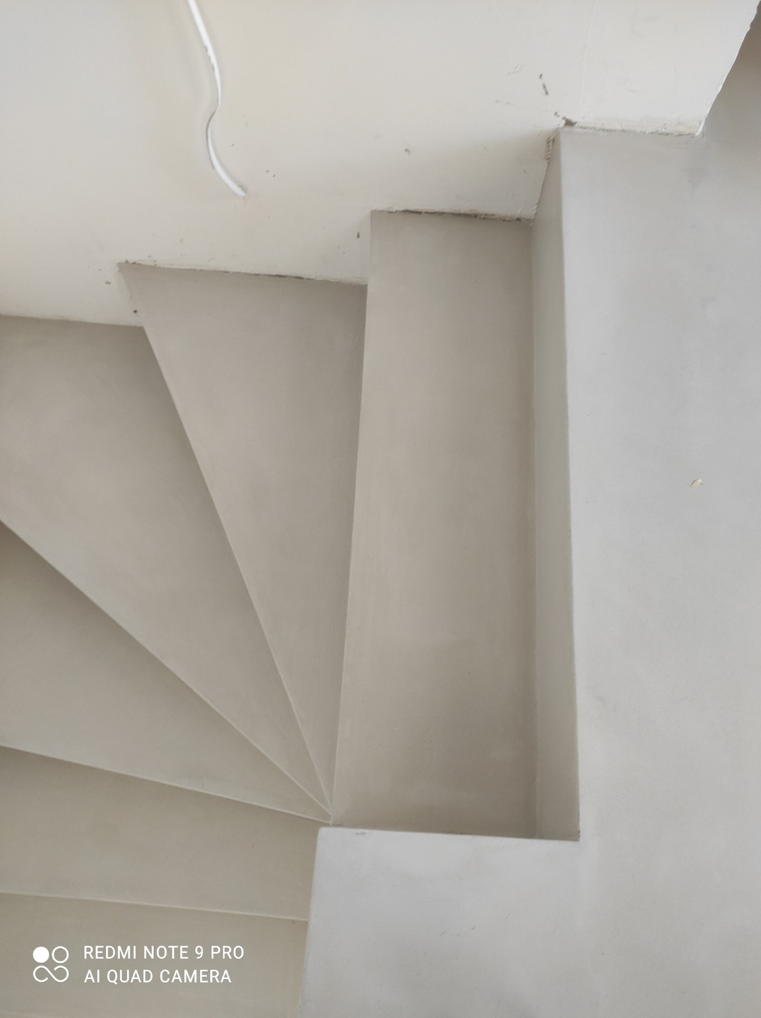 Schody wykończone jasnoszarym, gładkim materiałem, widok z góry, z widocznym kablem na suficie.