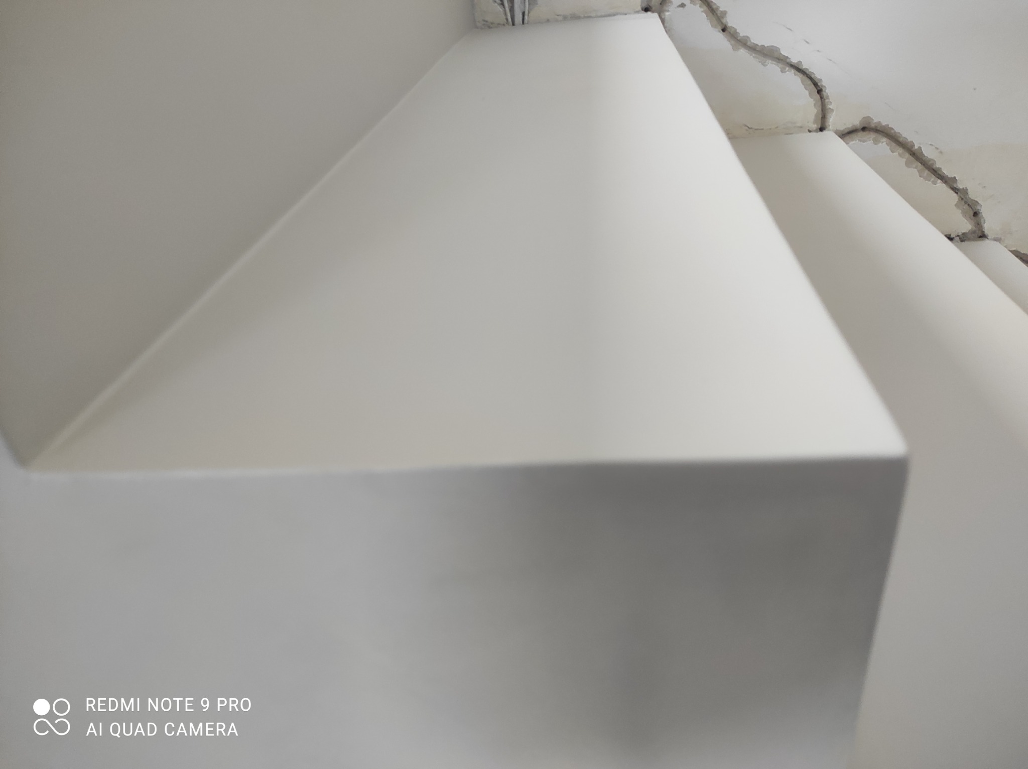 Świeżo nałożona, jasnoszara powłoka na ścianie z widocznymi śladami po szpachlowaniu na suficie w tle.