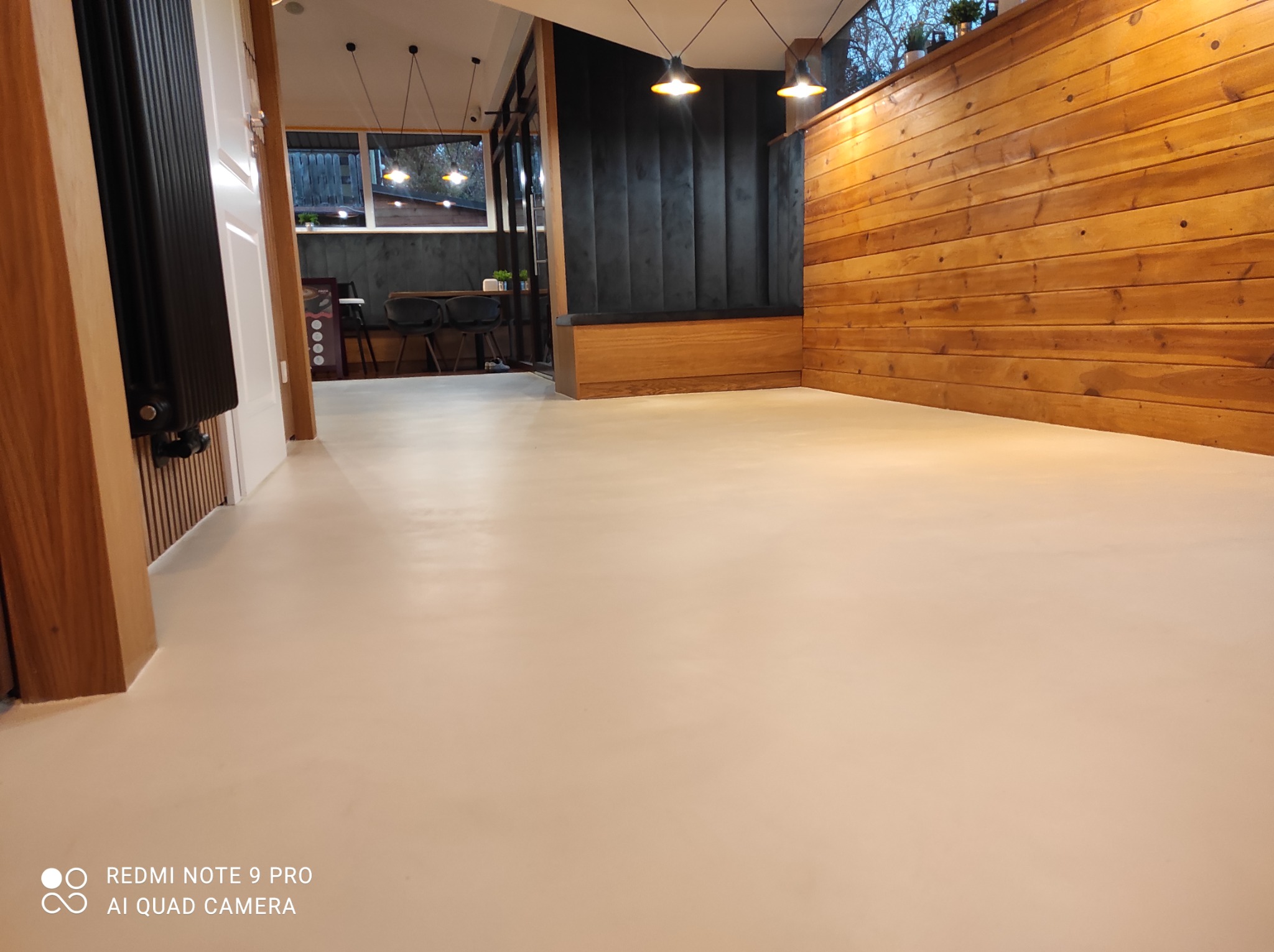 Jasna, gładka posadzka w nowocześnie urządzonym wnętrzu z drewnianą boazerią i ciemną tapicerowaną ścianą z wbudowanym siedziskiem.