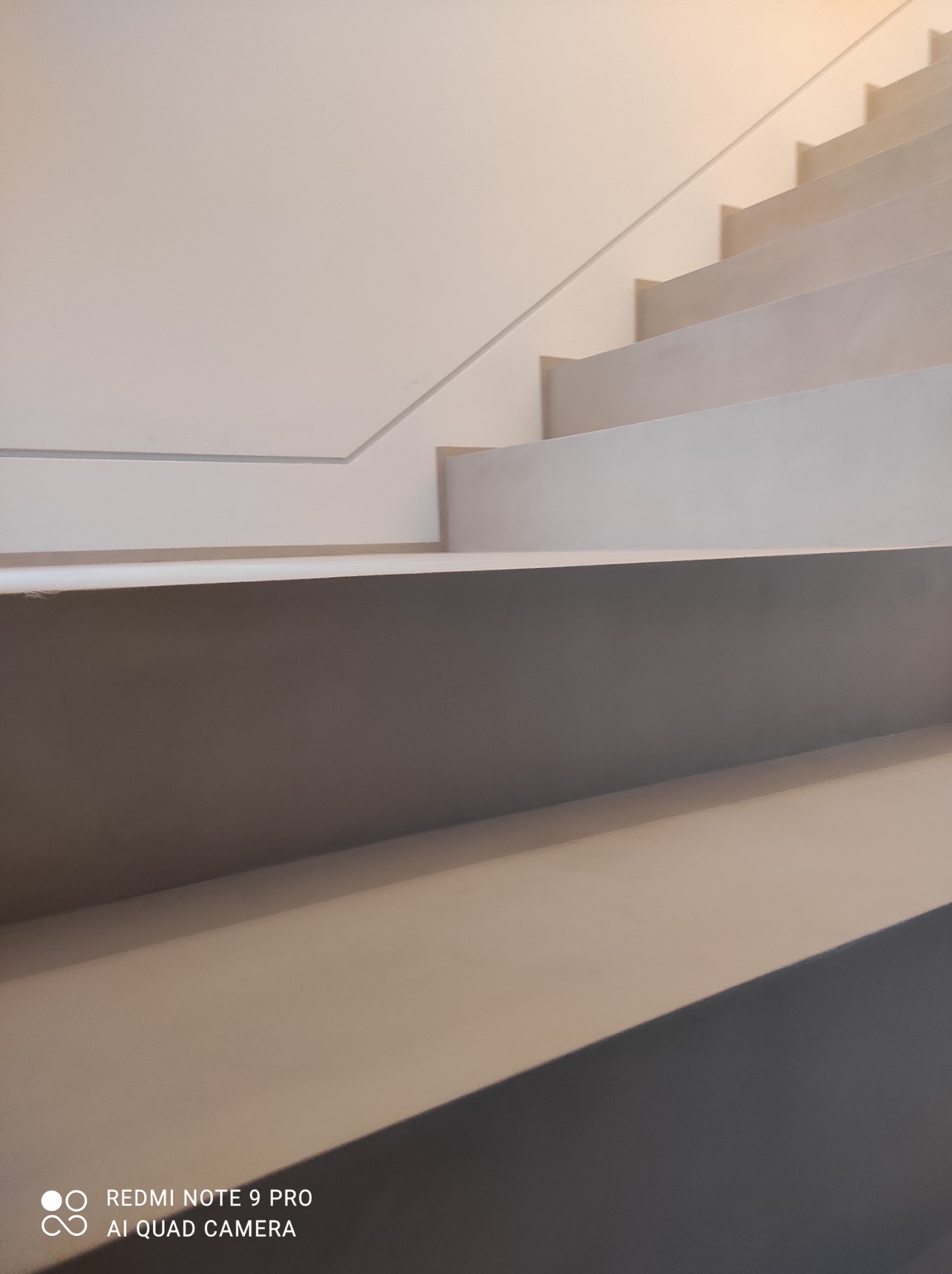 Schody wykończone jasnym, gładkim materiałem, prawdopodobnie mikrocementem, z minimalistyczną barierką w tle.