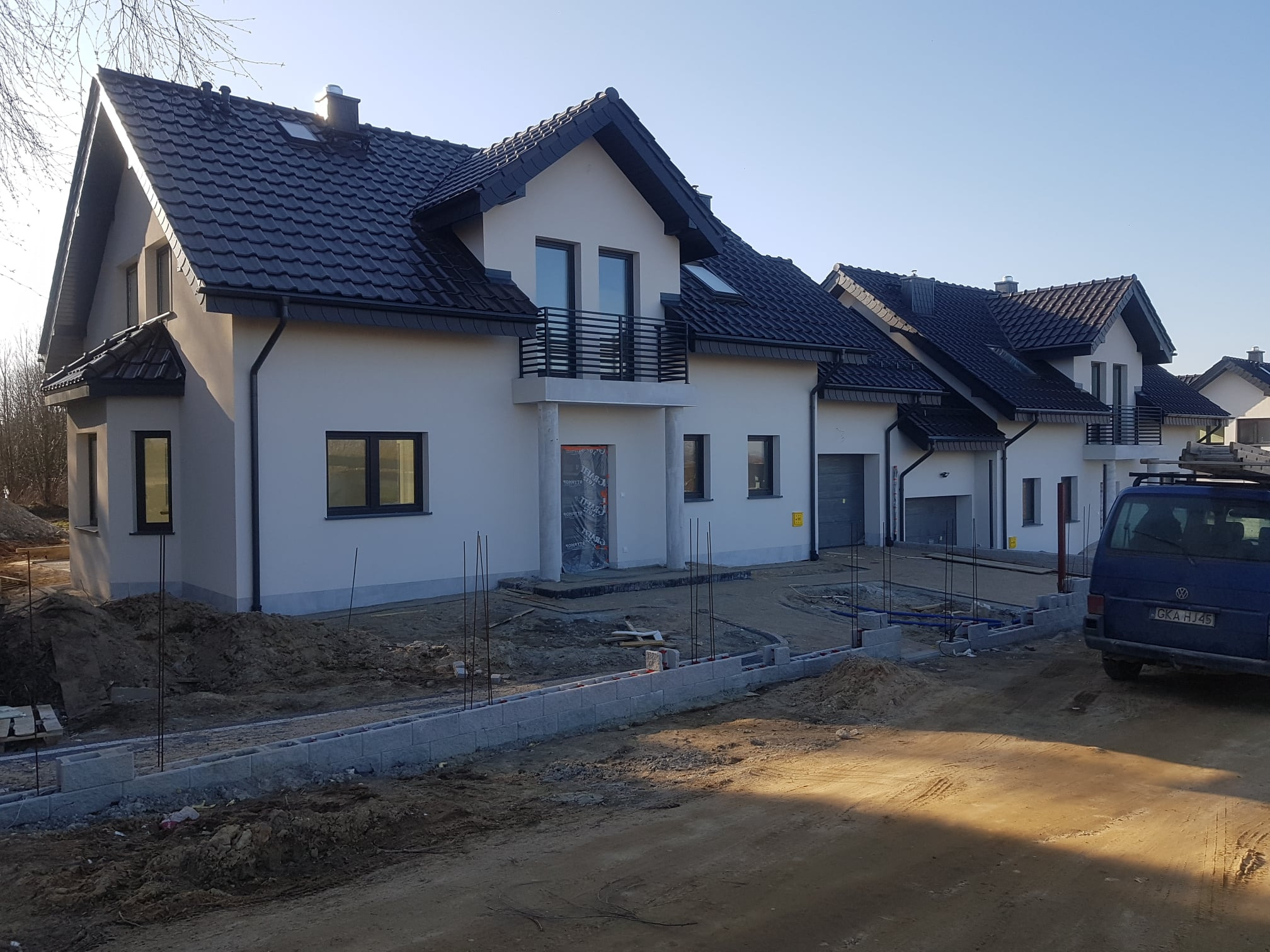 Nowe domy w Czaplach z ciemną dachówką i elementami obróbek blacharskich, teren wokół w trakcie zagospodarowywania.