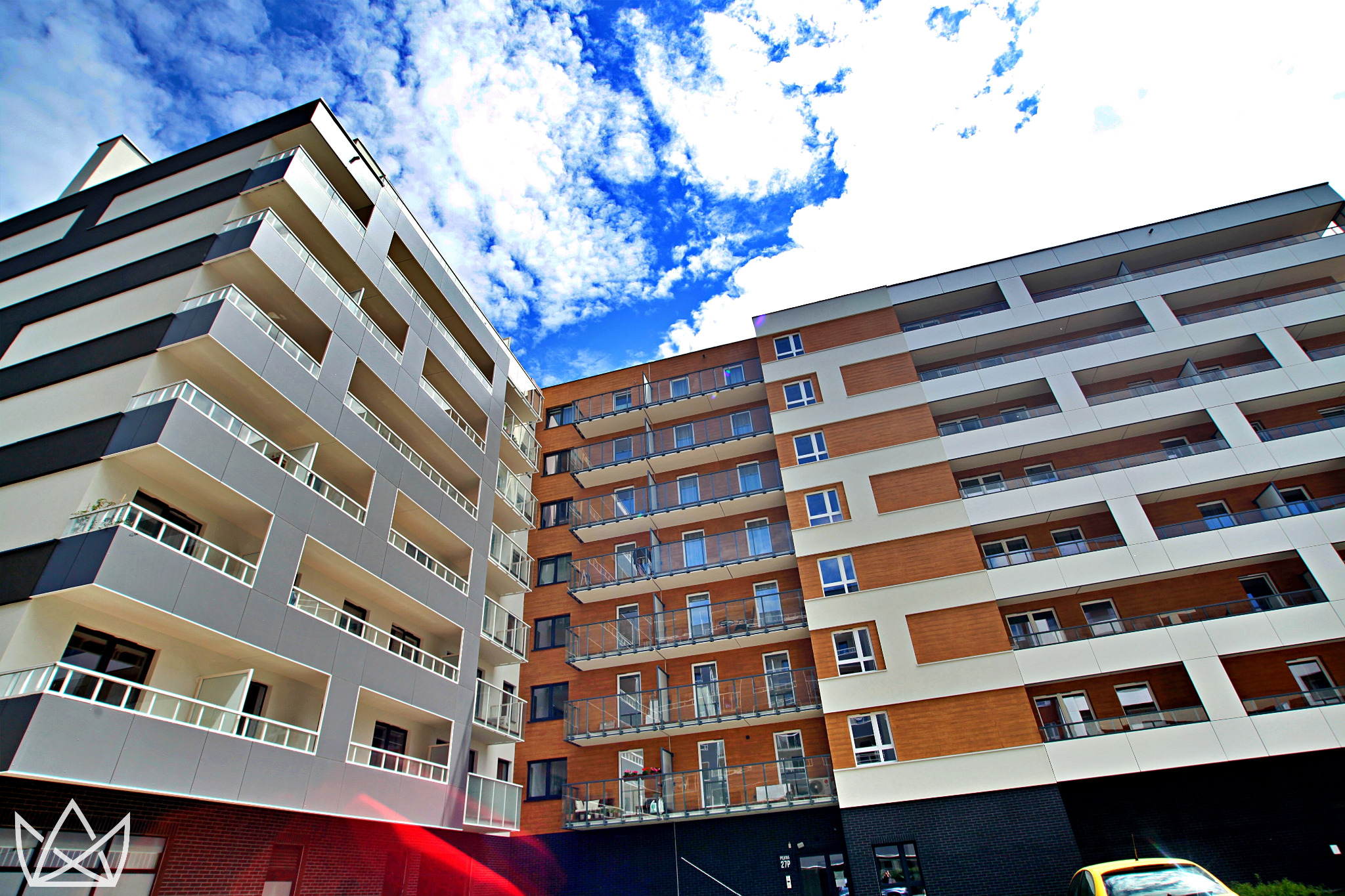 Nowoczesna architektura wielopiętrowego budynku mieszkalnego z balkonami, widok z dołu na błękitne niebo z chmurami.