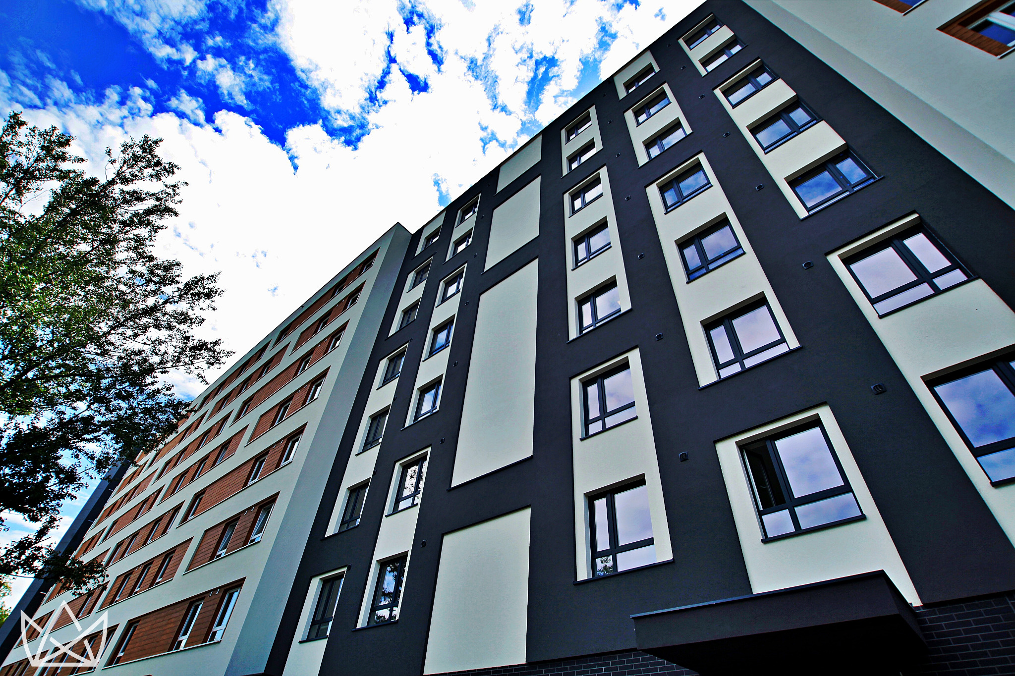 Wielopiętrowy budynek mieszkalny w Wołowie z nowoczesną elewacją, prezentujący okna o regularnym układzie na tle błękitnego nieba z chmurami.