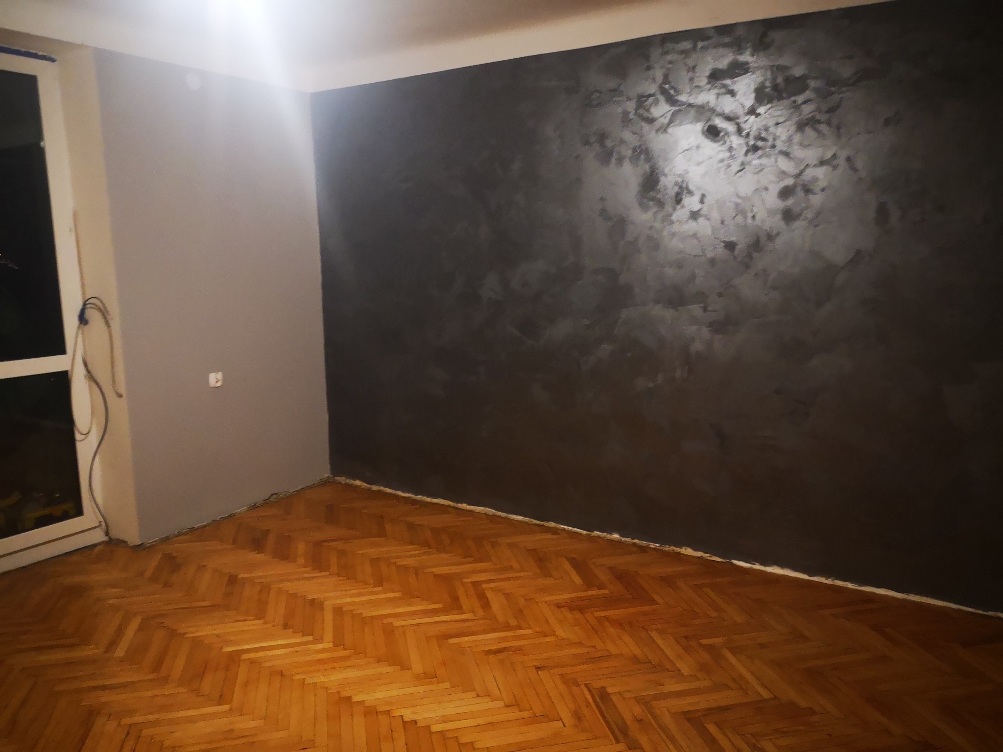 Pomieszczenie po malowaniu: jedna ściana szara, druga w ciemnym odcieniu szarości z efektem dekoracyjnym, parkiet ułożony w jodełkę.