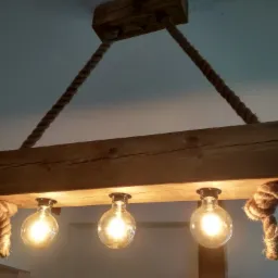 Drewniana lampa sufitowa w stylu rustykalnym, zawieszona na grubych linach jutowych, z trzema żarówkami Edisona