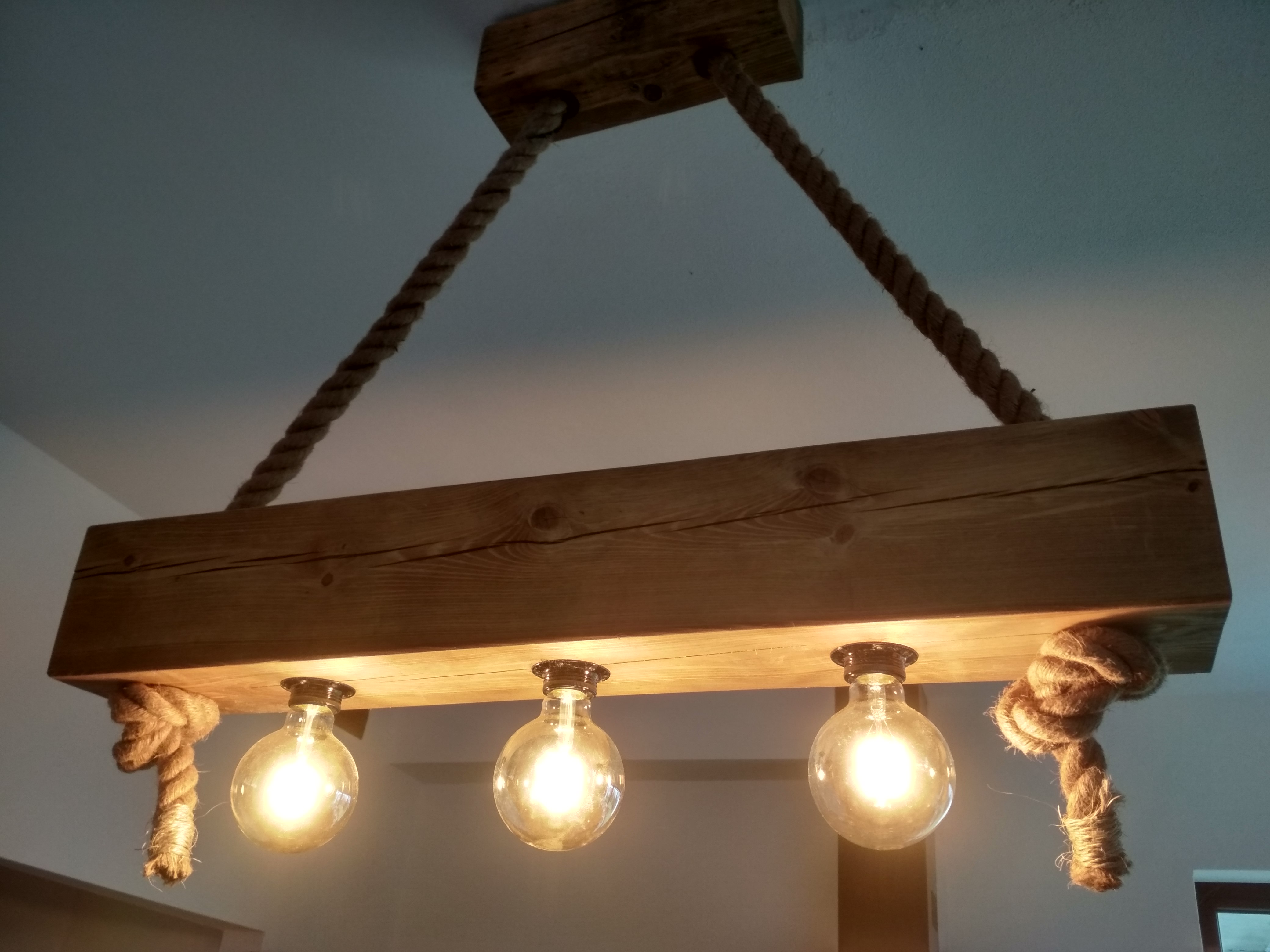 Drewniana lampa sufitowa w stylu rustykalnym, zawieszona na grubych linach jutowych, z trzema żarówkami Edisona