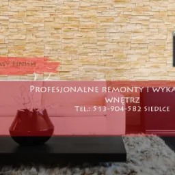 Salon z dekoracyjną ścianą z kamienia, sofa, stolik kawowy z wazonem, obraz na ścianie, reklama firmy remontowej.