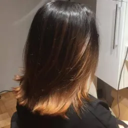 Tył głowy kobiety z włosami w odcieniach ciemnego brązu przechodzącego w miedziany blond na końcach, widoczne warstwowe cięcie.