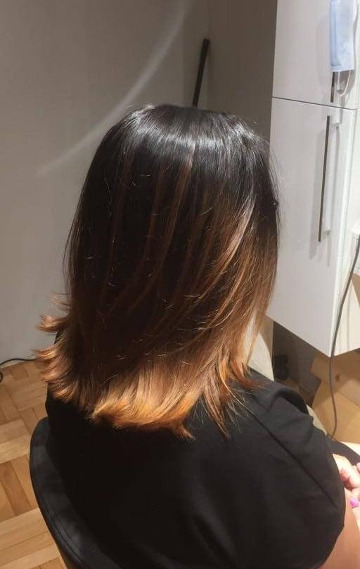 Tył głowy kobiety z włosami w odcieniach ciemnego brązu przechodzącego w miedziany blond na końcach, widoczne warstwowe cięcie.