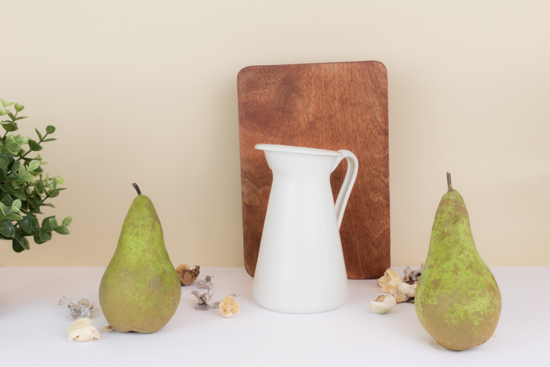 Martwa natura z dwiema gruszkami Forelle, białym dzbankiem, drewnianą deską i dekoracjami florystycznymi na białym stole.
