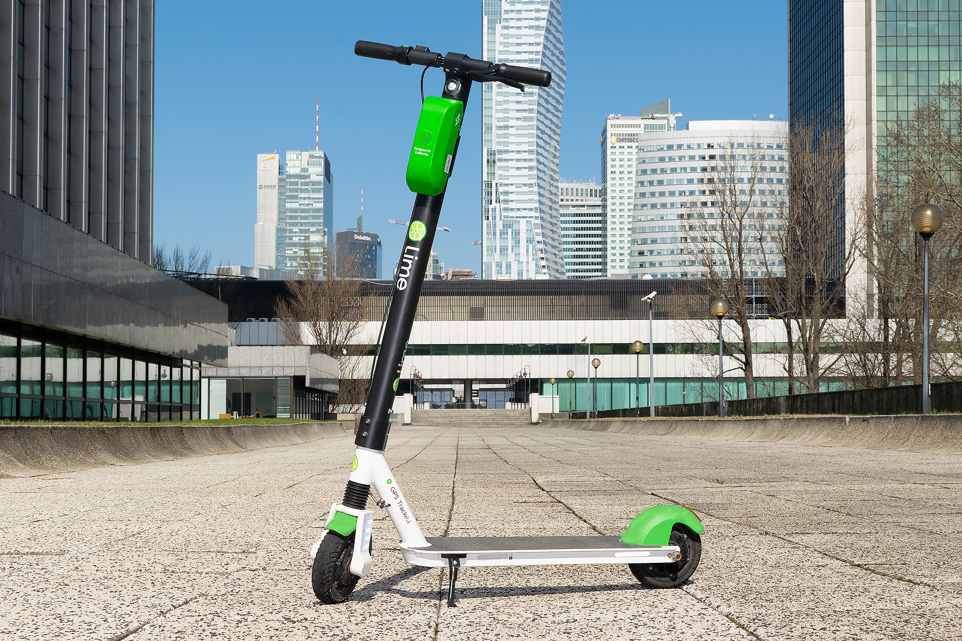 Elektryczna hulajnoga Lime zaparkowana na chodniku w centrum miasta, na tle wysokich budynków.