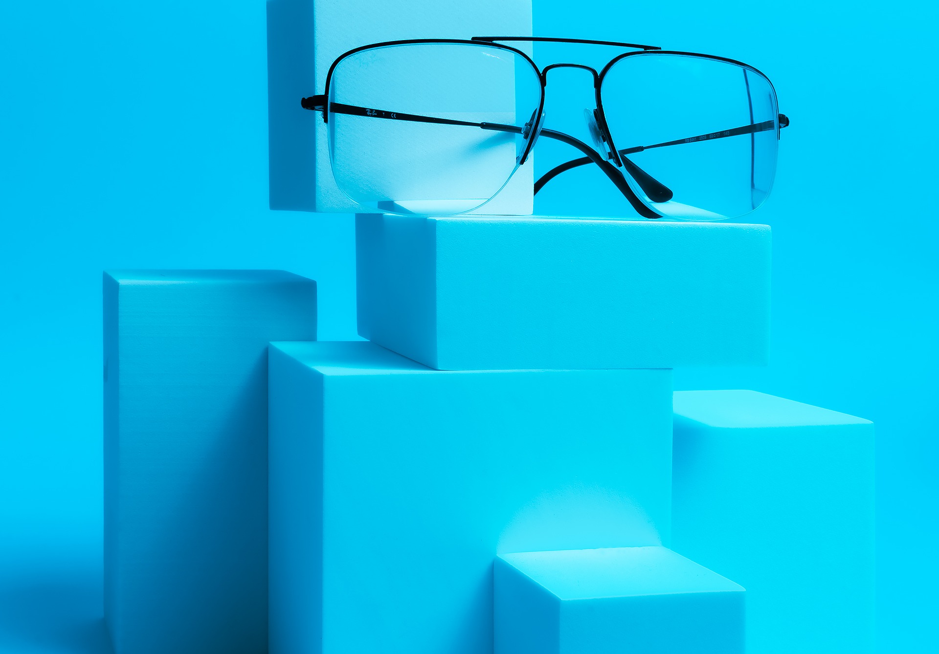 Okulary w czarnych oprawkach na tle piramidy z turkusowych sześcianów.