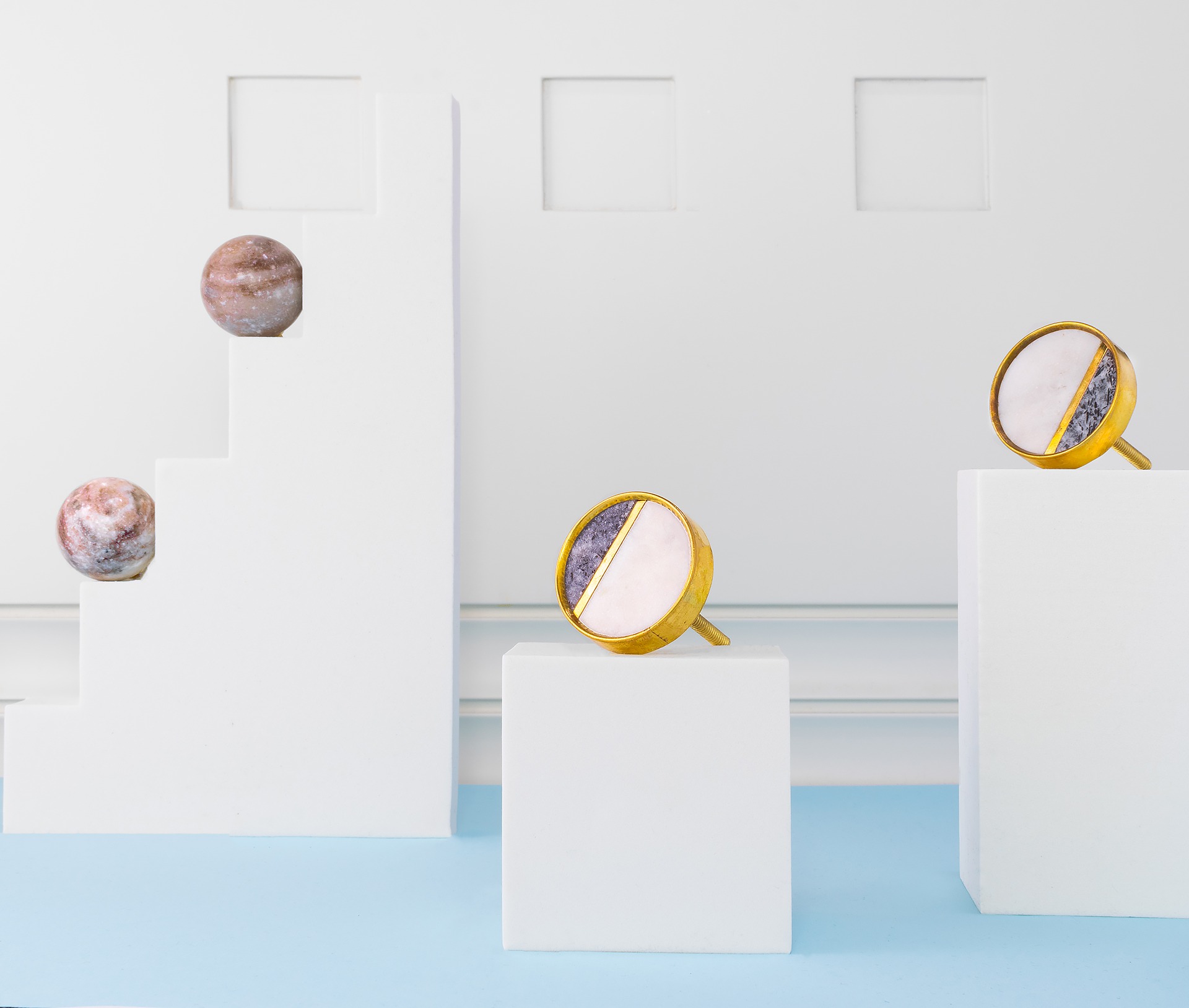 Dekoracyjne gałki do mebli z marmuru i złota na białych postumentach i minimalistycznym tle.