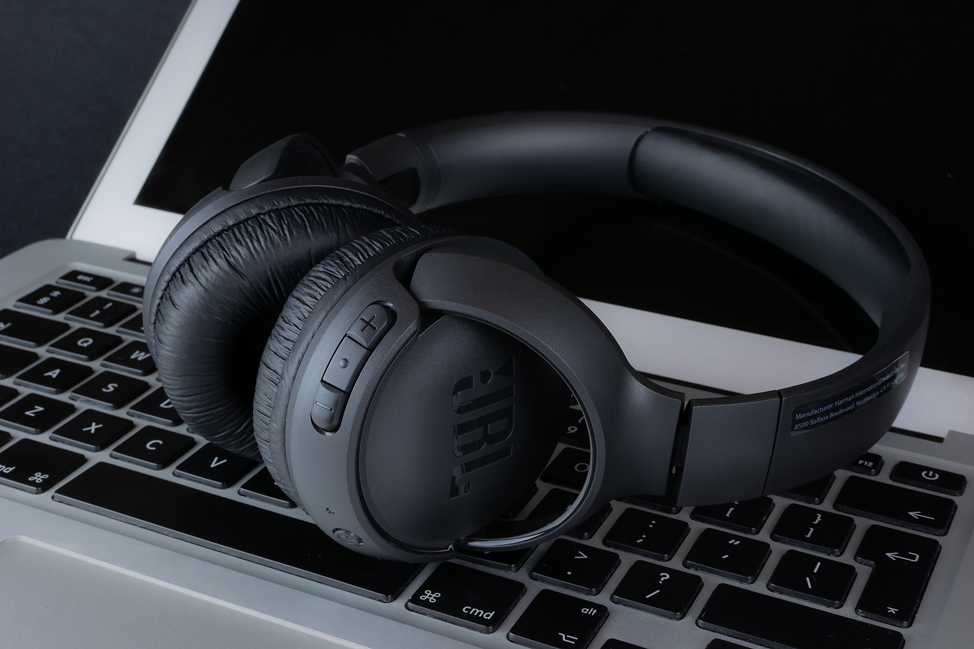 Czarne słuchawki JBL na klawiaturze laptopa z widocznym ekranem w tle.