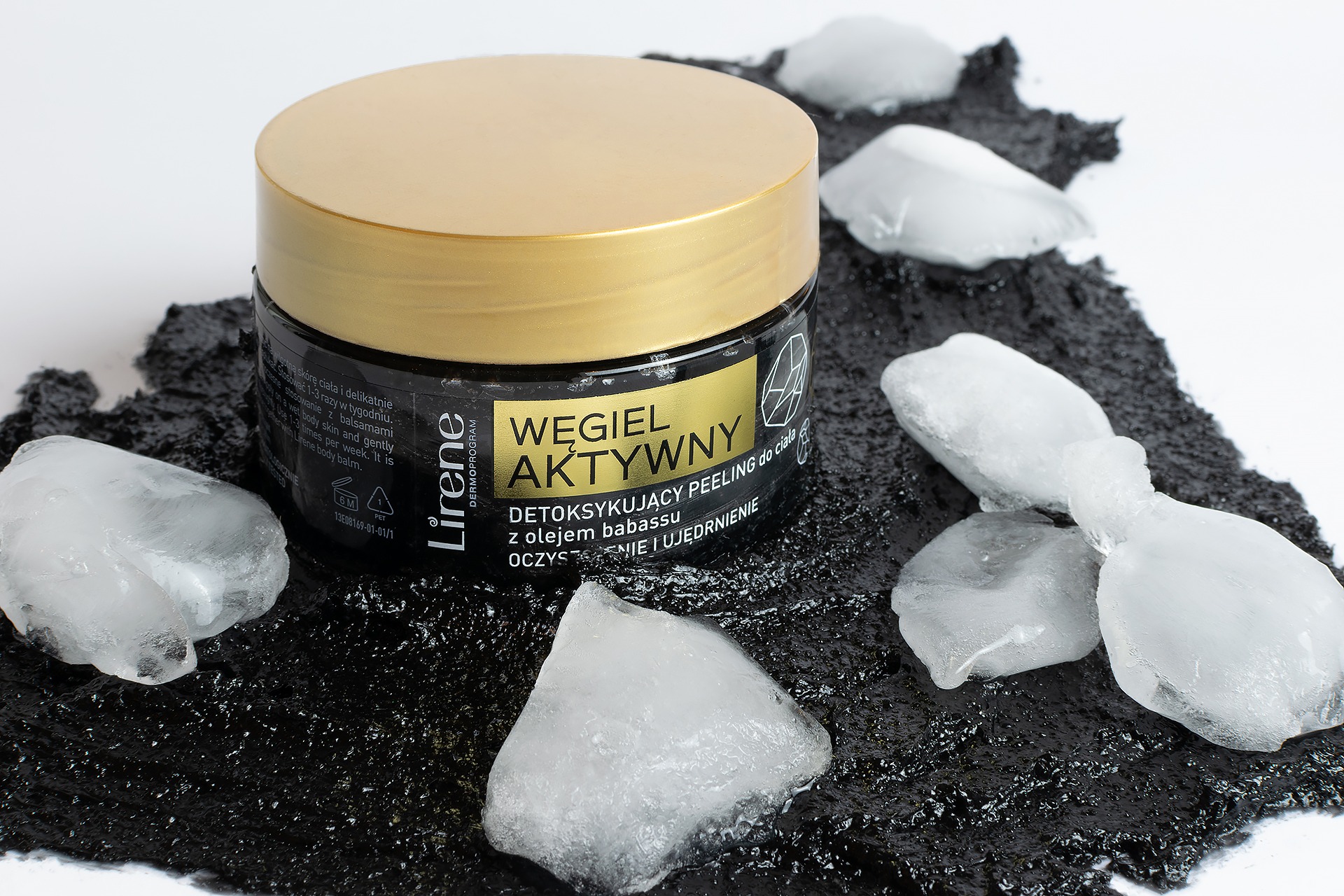 Słoik czarnego peelingu do ciała z węglem aktywnym marki Lirene, z złotą nakrętką, otoczony bryłkami lodu na czarnym, teksturowanym tle.