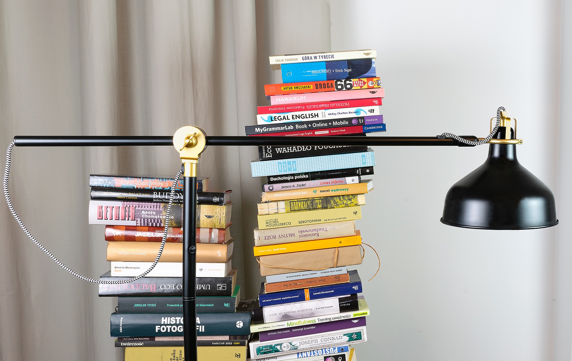 Czarna lampa biurkowa z elementami w kolorze złota, ustawiona na dwóch stosach książek, tworzących nietypową podstawę.