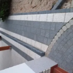 Ułożona kostka brukowa w odcieniach szarości i bieli, z obrzeżami z ciemniejszych kostek, widok z góry na fragment posesji.