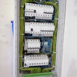 Rozdzielnica elektryczna w trakcie montażu, widoczne zabezpieczenia różnicowoprądowe Schneider Electric, przewody w peszlach i listwy zaciskowe, częściowo zamontowana w ścianie.