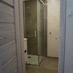 Perfect P - Nowoczesna łazienka z kabiną prysznicową, wykończona płytkami w odcieniach beżu i brązu, widok zza uchylonych drzwi z drewnopodobnym wykończeniem.