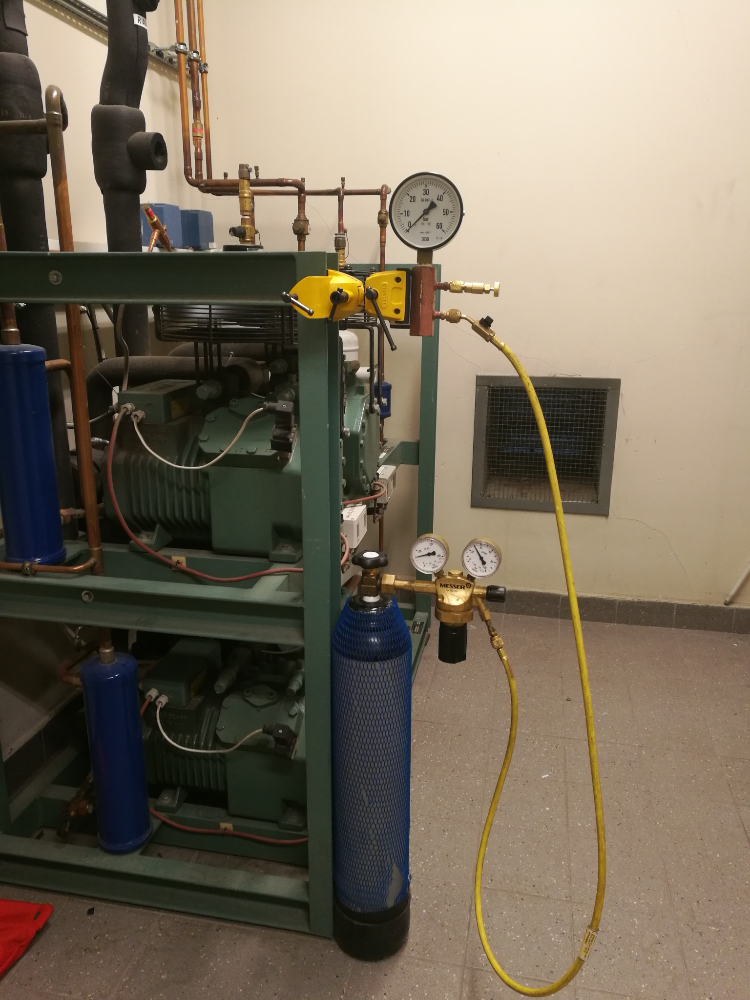 Instalacja chłodnicza z manometrami i butlą z gazem, widoczne rury miedziane i izolacja termiczna.