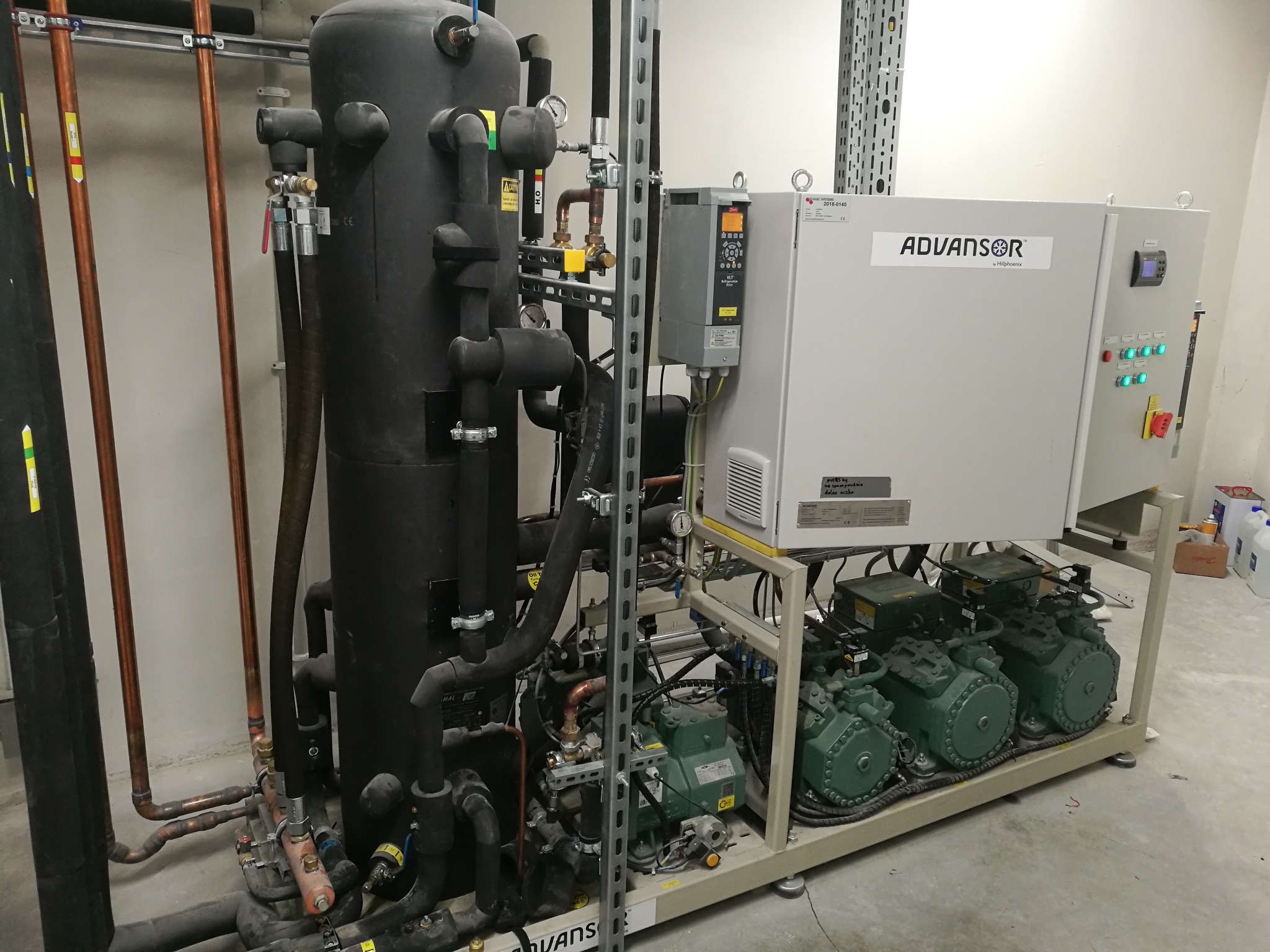 Przemysłowa instalacja chłodnicza Advansor z trzema zielonymi sprężarkami, zbiornikiem i panelami sterowania, widoczne rury miedziane i stalowe