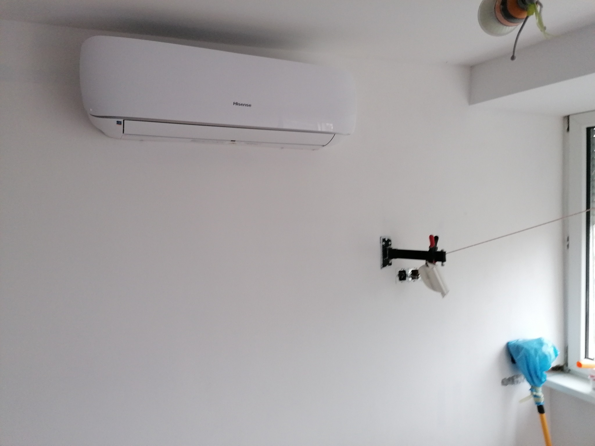 Biały klimatyzator Hisense zamontowany na świeżo pomalowanej ścianie, widoczne zabezpieczenia folią malarską i uchwyt na ścianie
