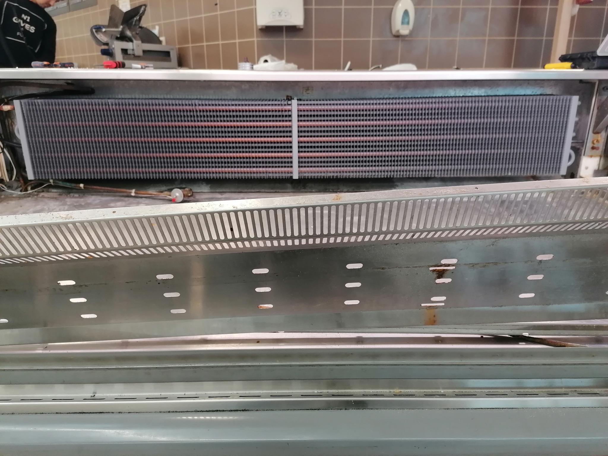 Wnętrze chłodni sklepowej z widocznym parownikiem i elementami instalacji chłodniczej, podczas prac serwisowych.