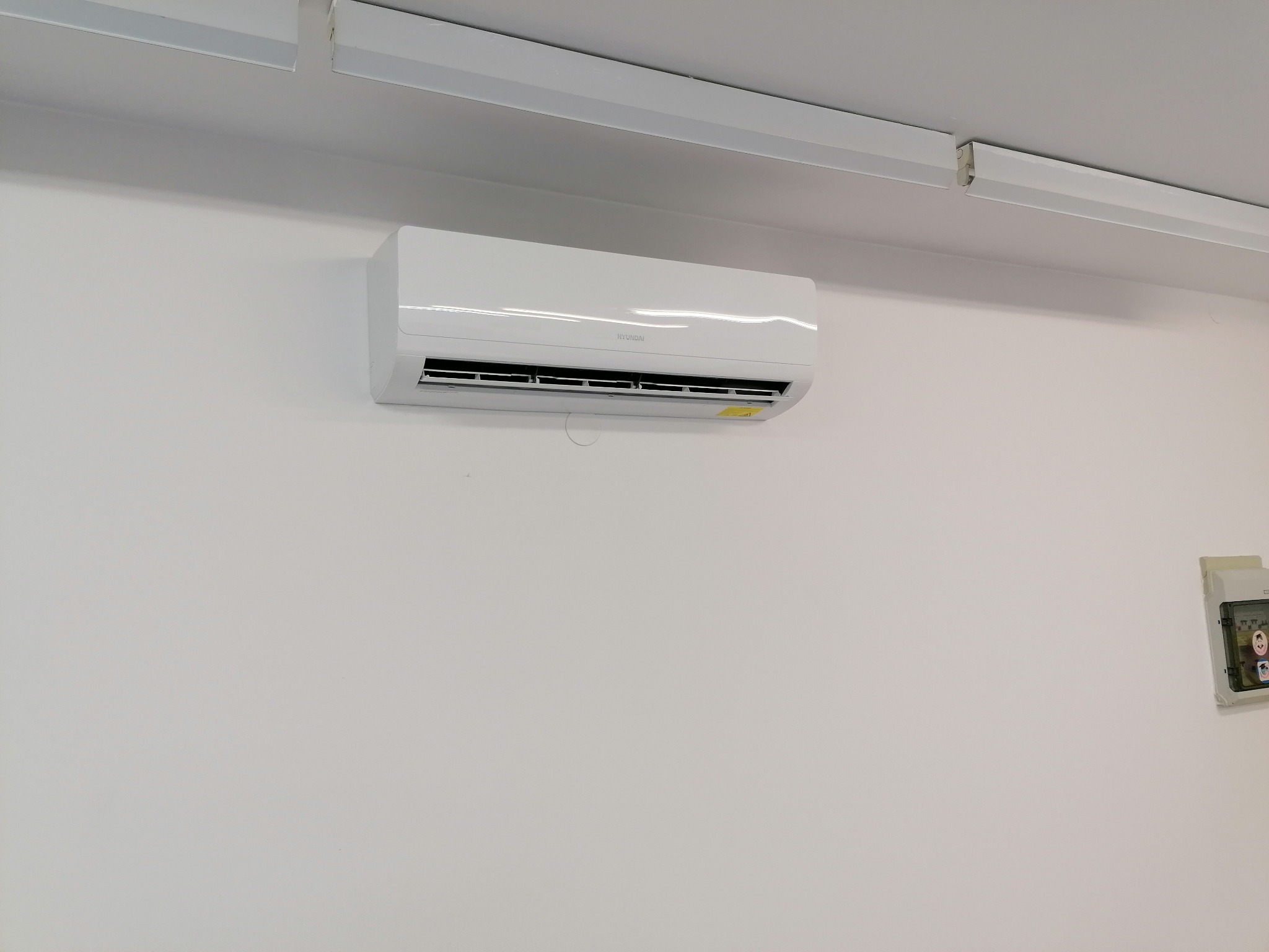 Biały klimatyzator marki Hyundai zamontowany na białej ścianie pod sufitem z oświetleniem ledowym.