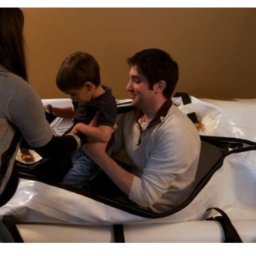 Hiperbaryczne Komory Tlenowe mHBOT Polska - Mężczyzna z uśmiechem na twarzy umieszcza małe dziecko w białej, nadmuchiwanej komorze w Katowicach, podczas gdy druga osoba asystuje.