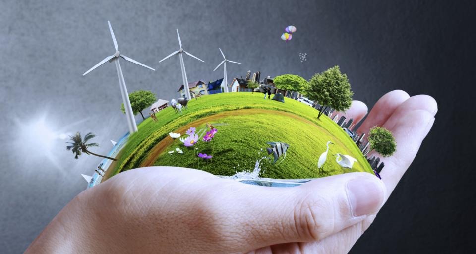 Miniaturowy krajobraz z turbinami wiatrowymi i domami, trzymany w dłoni, symbolizujący zrównoważony rozwój i odnawialne źródła energii.