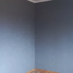 Pusta, pomalowana na szaro ściana pokoju z drewnianą podłogą i wiszącą lampą z mlecznymi kloszami.