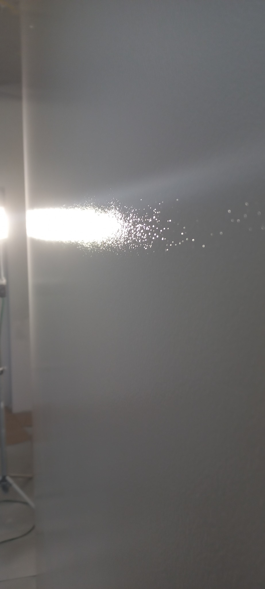 Świeżo pomalowana ściana oświetlona lampą halogenową, ukazująca delikatną strukturę farby.