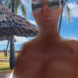 Mężczyzna w okularach przeciwsłonecznych na tle tropikalnej plaży z palmami i parasolem ze strzechy, z efektem rozmycia i filtrem na twarzy.