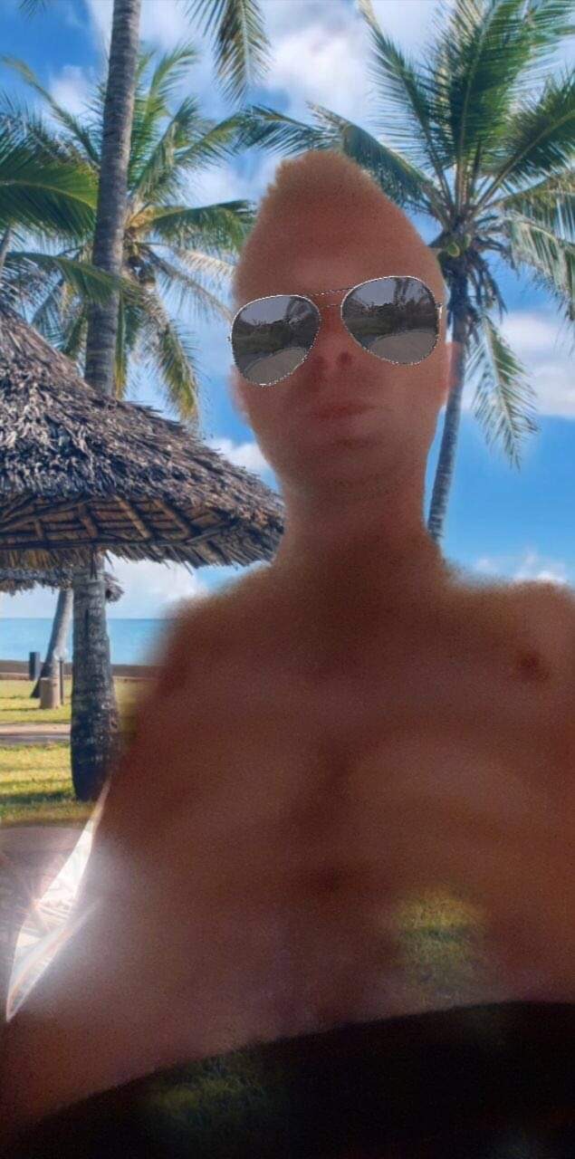 Mężczyzna w okularach przeciwsłonecznych na tle tropikalnej plaży z palmami i parasolem ze strzechy, z efektem rozmycia i filtrem na twarzy.