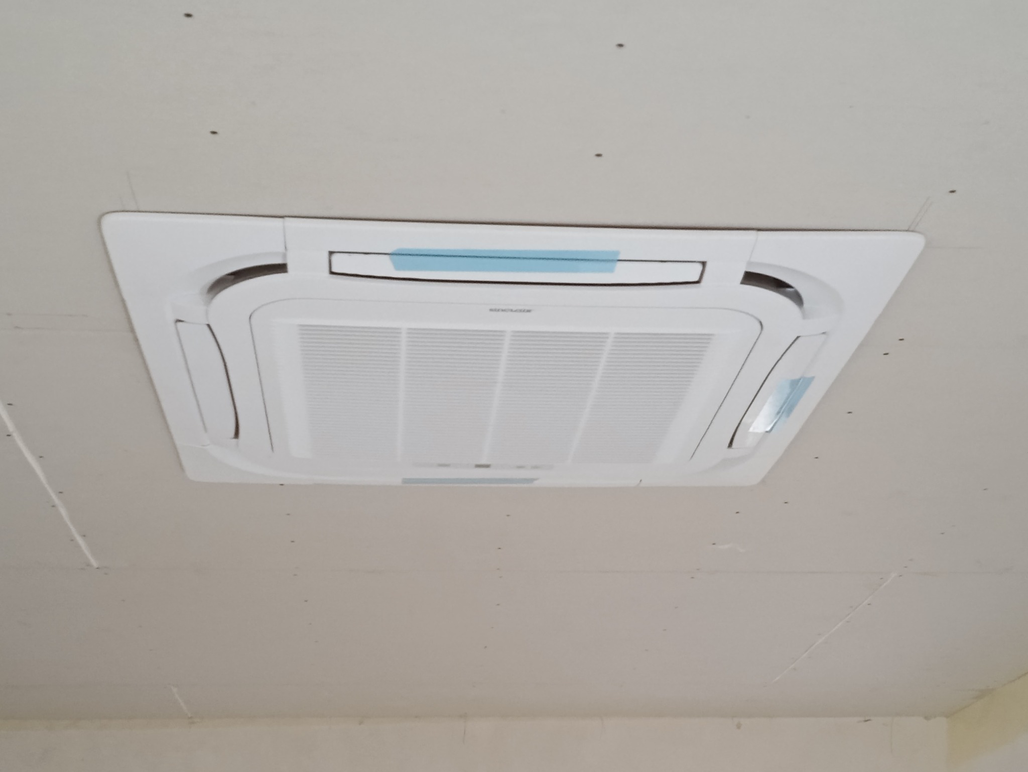 Kasetonowa jednostka wewnętrzna klimatyzacji zamontowana w suficie podwieszanym, zabezpieczona niebieską taśmą. Widoczne ślady po montażu na płycie gipsowej.