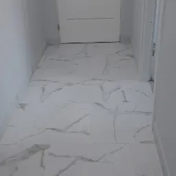 Wyłożona marmurowymi płytkami podłoga w przedpokoju, z widoczną białą, nowoczesną stolarką drzwiową i listwami przypodłogowymi.