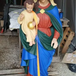 Figurka Matki Boskiej z Dzieciątkiem po renowacji, z widocznymi świeżymi warstwami farby i paskiem zabezpieczającym, umieszczona na palecie w warsztacie.