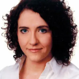 Portret kobiety o kręconych, ciemnych włosach i jasnych, niebieskich oczach, ubrana w białą koszulę.