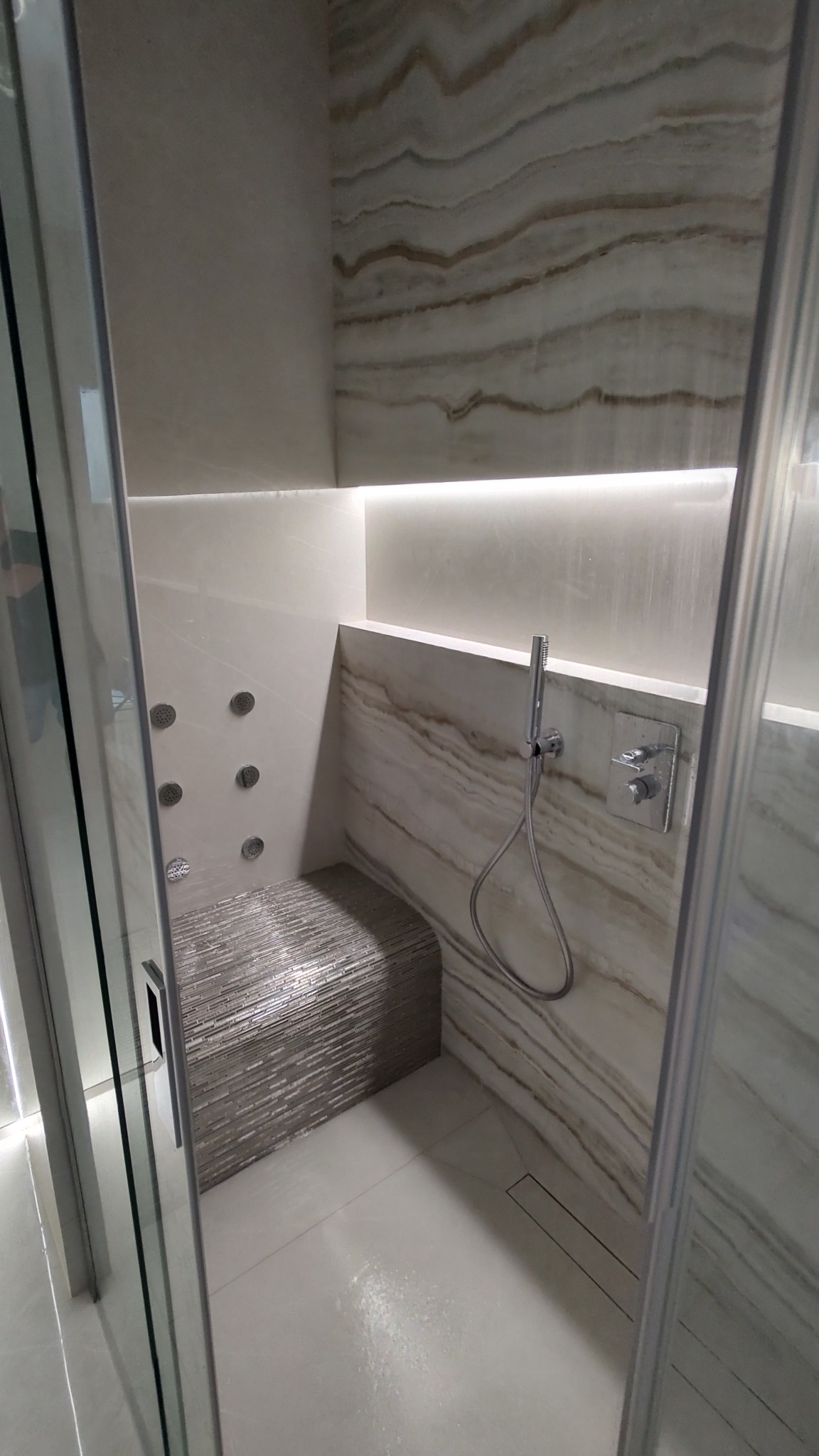 Nowoczesna kabina prysznicowa z siedziskiem wyłożonym mozaiką, panel z hydromasażem i armatura w kolorze chrom, oświetlenie LED.