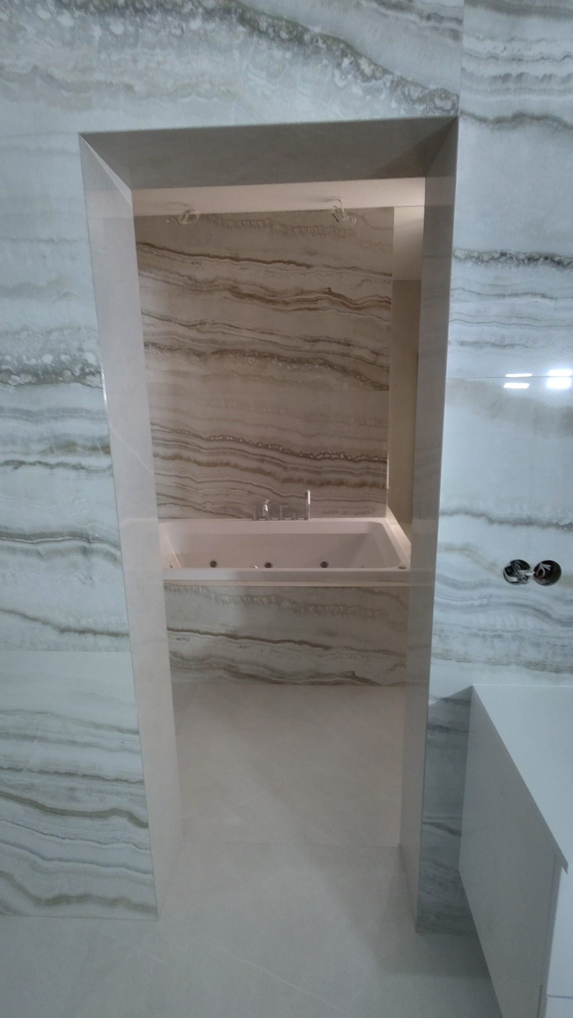 Wnęka w ścianie wyłożona płytkami imitującymi marmur, z widoczną wanną z hydromasażem i wystającymi elementami instalacji elektrycznej.