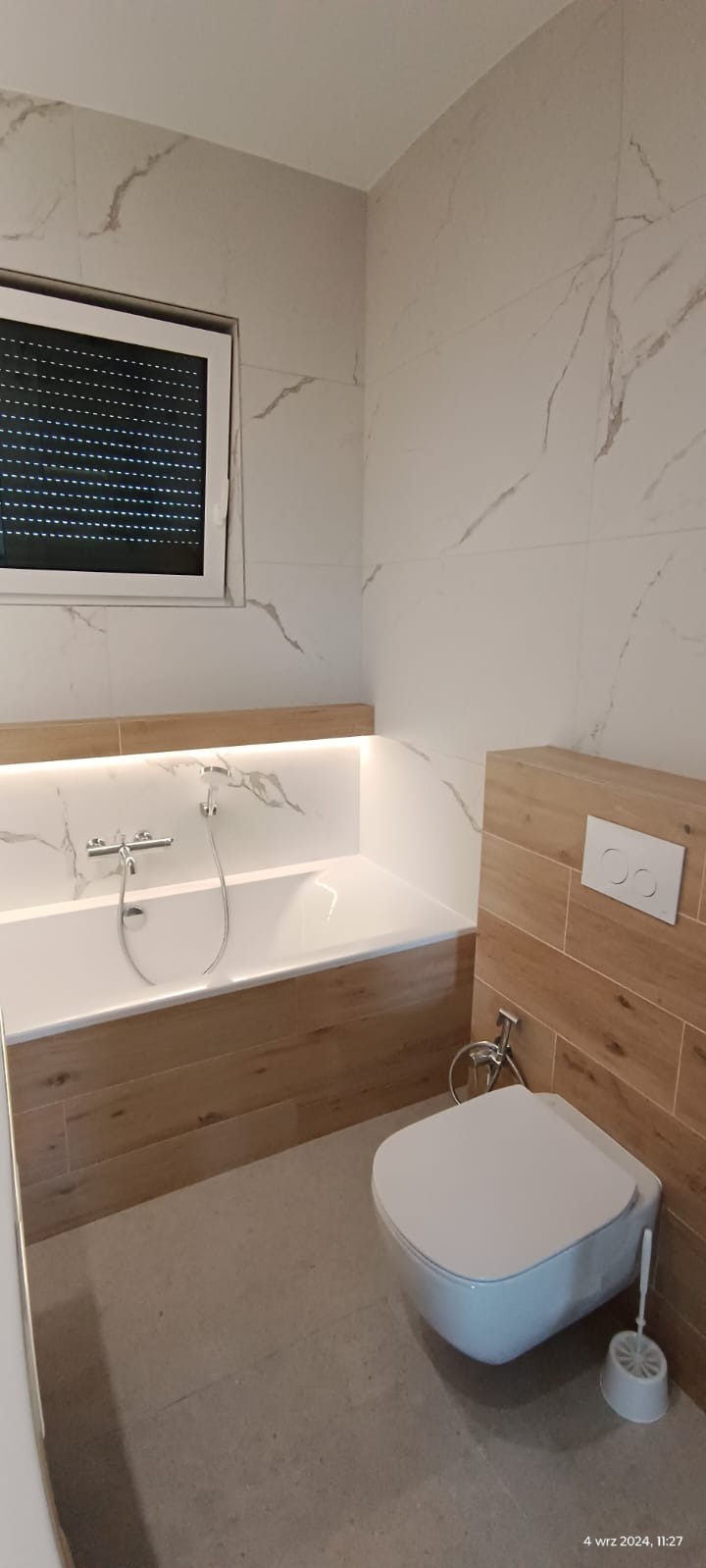 Nowoczesna łazienka z wanną w zabudowie z podświetleniem LED, toaleta podwieszana z bidetką i płytki imitujące marmur na ścianach.