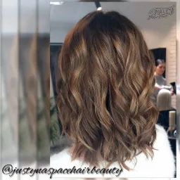 Koloryzacja brązowych, falowanych włosów z refleksami w salonie fryzjerskim w Nowym Sączu, widok z tyłu głowy.